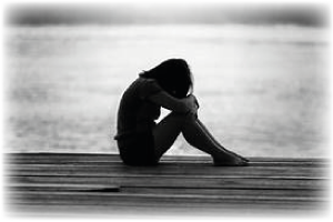 A person sitting, leaning forwards with head on their knees on a wooden pier